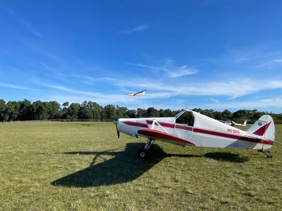 Tug aircraft VH-SMS on the airfield with a glider soaring above